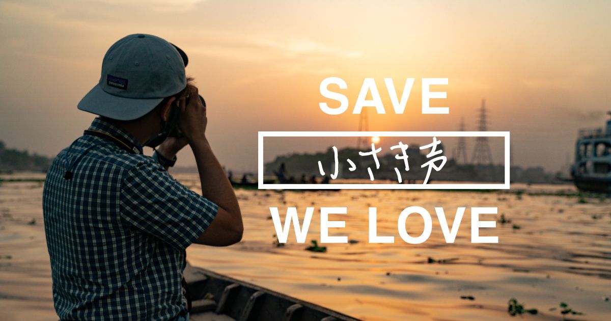 夕日を背にカメラを構える人物と「SAVE 小さき声 WE LOVE」の文字